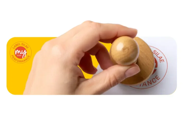 Illustration symbolisant la validation et la reconnaissance officielle : une main apposant un tampon sur un document avec le logo Label Silae My Performance sur fond jaune.