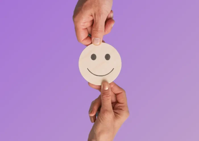 Deux mains tiennent un smiley en bois sur fond violet, symbole de feedback positif en entreprise